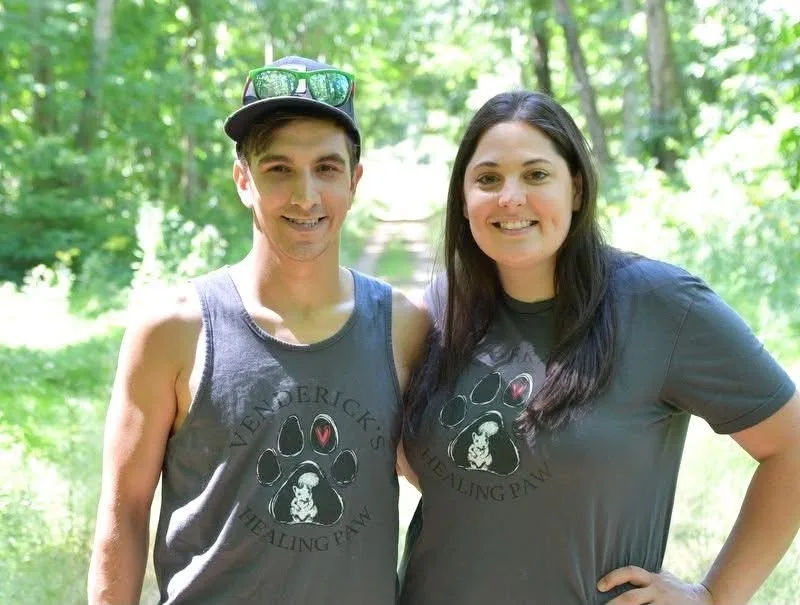 Brittany and Ryan smiling together in Venderick's Healing Paw shirts on a wooded trail